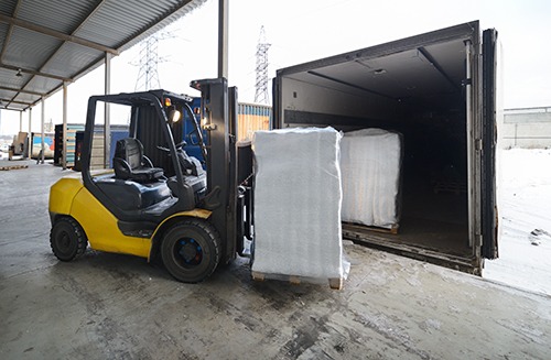 Forklift in warehouse loading dig box into a car outdoors
